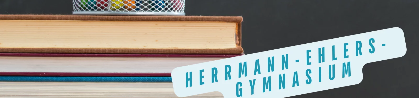 Stapel von Büchern mit einem Stiftehalter im Hintergrund, daneben steht in großen, blauen Buchstaben 'Herrmann-Ehlers-Gymnasium' auf einem hellblauen Banner.