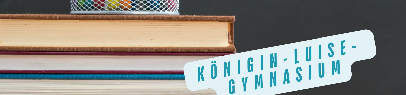 Stapel von Büchern mit einem Behälter für Stifte, daneben ein Schild mit der Aufschrift Königin-Luise-Gymnasium.
