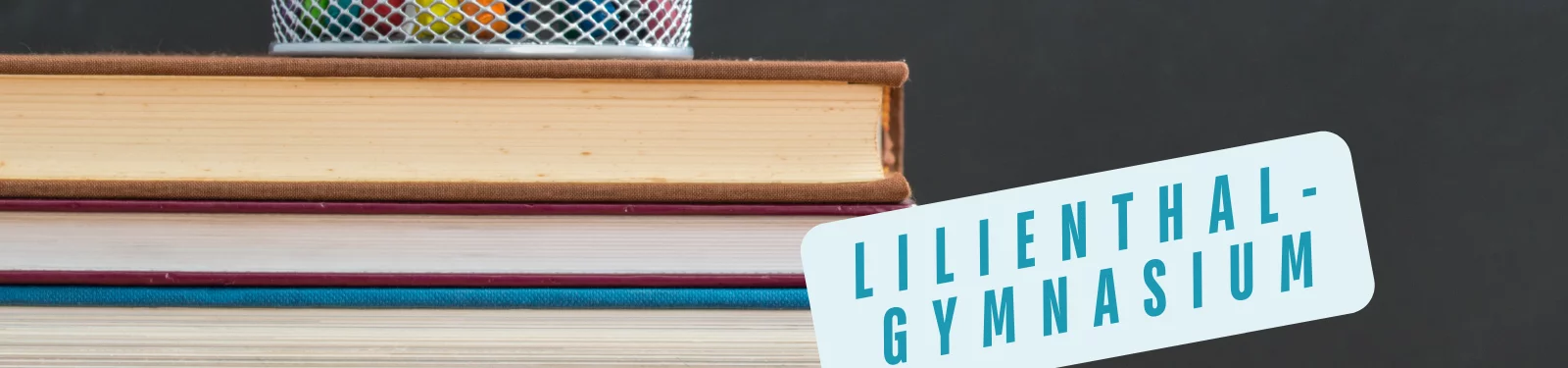Ein Stapel Bücher mit einem Stiftehalter darauf, daneben ein Schild mit der Aufschrift "Lilienthal-Gymnasium".