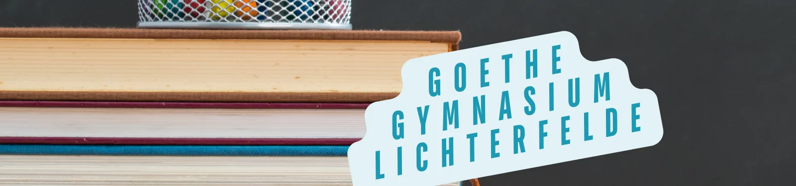 Ein Stapel Bücher mit einem Stiftehalter darauf. Ein Schild zeigt den Text "Goethe Gymnasium Lichterfelde"