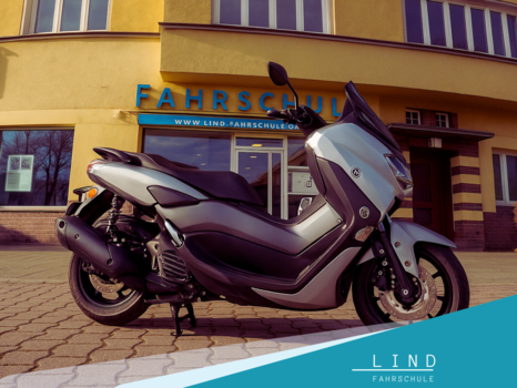 Silberner Yamaha NMAX Roller vor der Fahrschule Lind in Berlin am Breitenbachplatz, aufgenommen bei Sonnenschein – modernes Ausbildungsfahrzeug für B196 und Rollerführerschein.