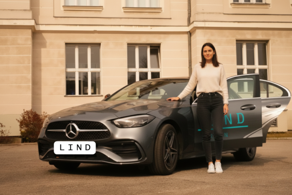 Junge Frau steht neben einem Mercedes-Fahrschulfahrzeug der Fahrschule Lind in Berlin vor einem Gebäude. geöffnete Autotür, modernes Ausbildungsfahrzeug.