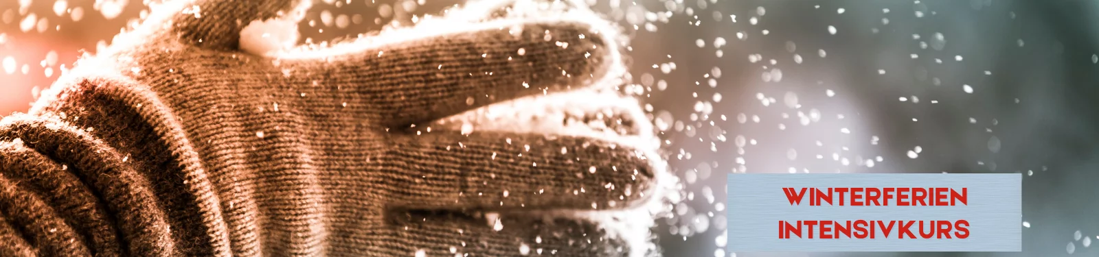 Winterliches Werbemotiv für den Winterferien-Intensivkurs: Nahaufnahme einer braunen Strickhandschuh-Hand, die Schnee in die Luft wirft, während Schneeflocken im warmen Licht glitzern. Rechts im Bild steht auf einer hellen Fläche in roter Schrift „Winterferien Intensivkurs“.