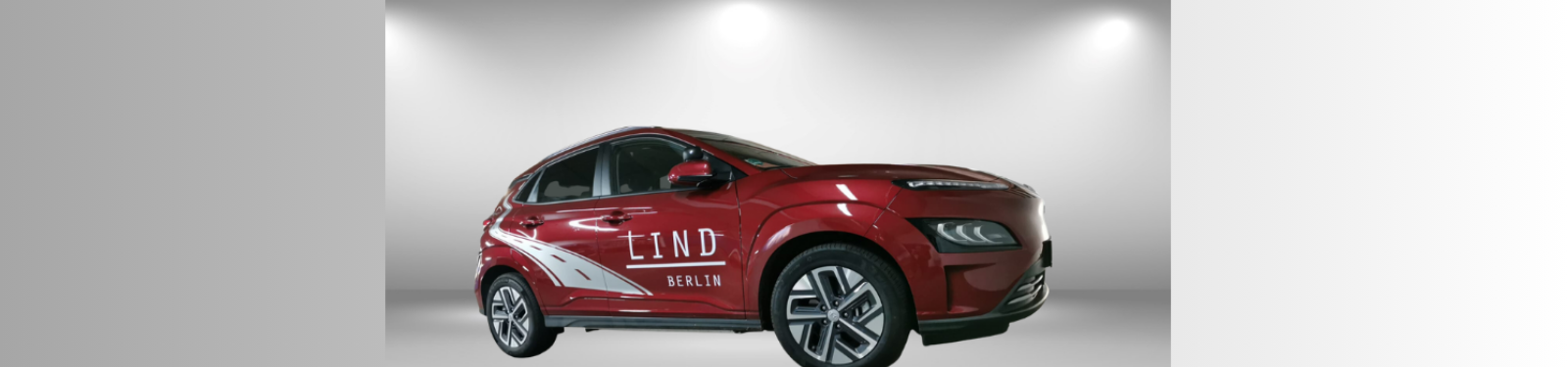 Rotes Elektroauto mit der Aufschrift 'LIND BERLIN' an der Seite, ausgestellt unter hellem Studiolicht.