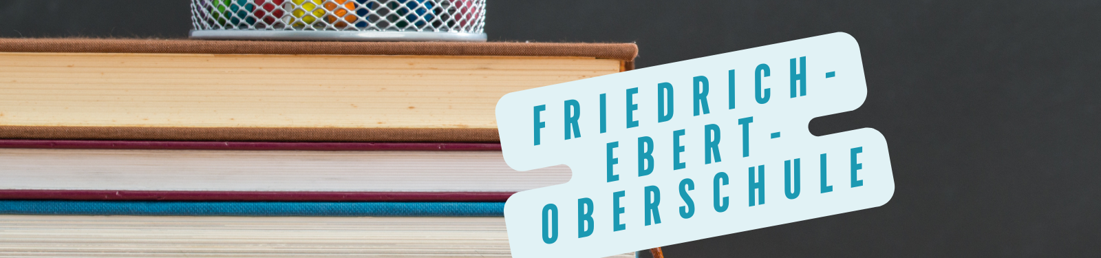 Ein Stapel Bücher mit einem Stiftehalter obenauf. Rechts davon befindet sich ein Schild mit der Aufschrift "Friedrich-Ebert-Oberschule".