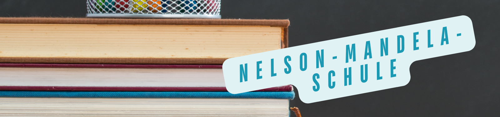 Stapel von Büchern mit einem Etikett, das den Text 'Nelson-Mandela-Schule' trägt, vor einem dunklen Hintergrund.