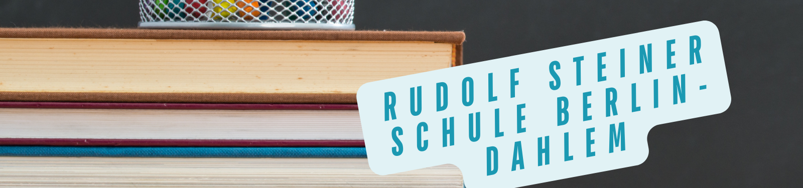 Ein Stapel Bücher mit einem Stiftehalter auf einem Tisch. Auf einem blauen Etikett steht 'Rudolf Steiner Schule Berlin-Dahlem'