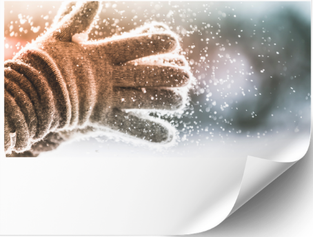 Winterliches Motiv mit umgeschlagener Papierecke: Eine braune Strickhandschuh-Hand wirft Schnee in die Luft, feine Schneeflocken glitzern vor einem unscharfen, kühlen Hintergrund. Der untere Bereich des Bildes ist hell gestaltet und wirkt wie eine umgeblätterte Seite.